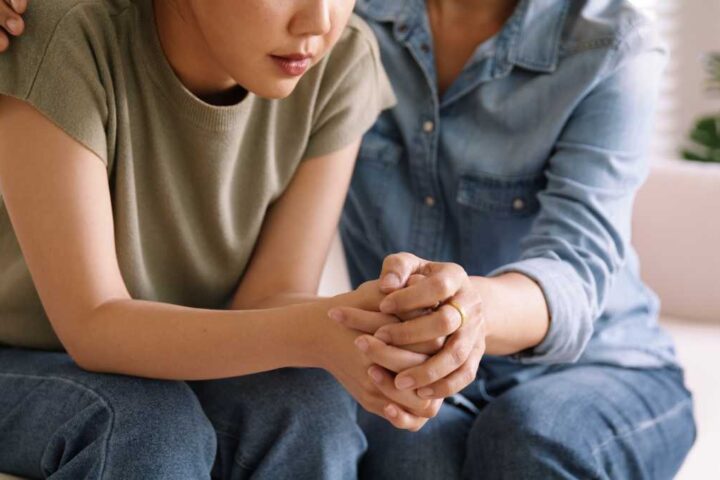 Person receiving emotional support from another individual, with their hands clasped together in a moment of connection, representing therapeutic relationships that benefit sensitive individuals.