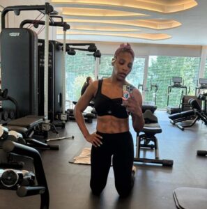 Serena Williams taking a mirror selfie in a gym wearing black workout attire, showing her toned abdomen and physique.