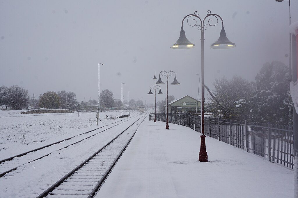 Snow-covered railway tracks and platform at Orange railway station, New South Wales, Australia. Ornamental lamp posts line the tracks, and snow blankets the surrounding area creating white-out conditions.