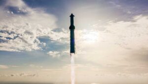 SpaceX Starship rocket ascending through clouds with engine firing during Flight 10 test, silhouetted against a bright blue sky with scattered white clouds.