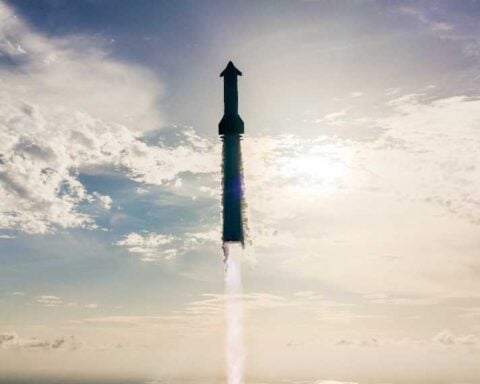 SpaceX Starship rocket ascending through clouds with engine firing during Flight 10 test, silhouetted against a bright blue sky with scattered white clouds.