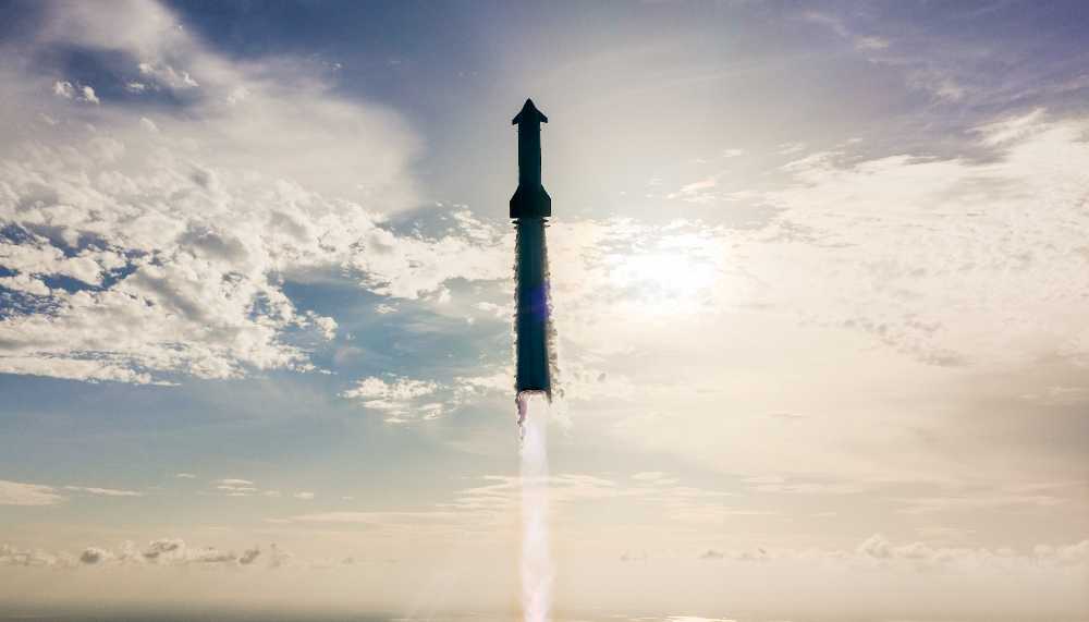 SpaceX Starship rocket ascending through clouds with engine firing during Flight 10 test, silhouetted against a bright blue sky with scattered white clouds.
