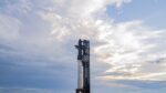Fully stacked Starship and Super Heavy rocket at the launch pad under cloudy skies, with vapors surrounding the base as it awaits the Flight 10 test.