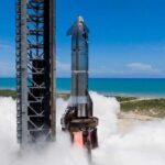 Starship on Pad 1 at Starbase during single‑engine static fire with exhaust plume, ocean and clear sky in background
