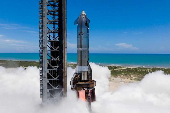 Starship on Pad 1 at Starbase during single‑engine static fire with exhaust plume, ocean and clear sky in background
