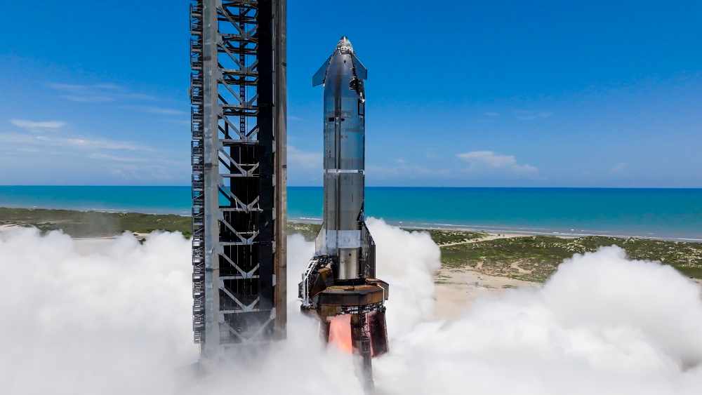Starship on Pad 1 at Starbase during single‑engine static fire with exhaust plume, ocean and clear sky in background