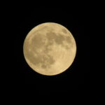 Golden full Sturgeon Moon glowing against a pitch-black sky.