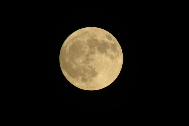 Golden full Sturgeon Moon glowing against a pitch-black sky.