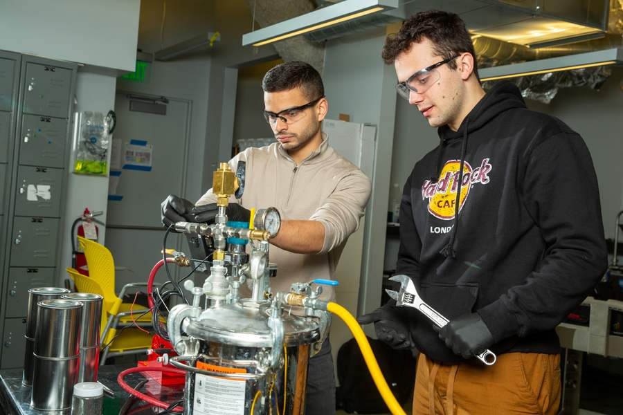 MIT engineers Aly Kombargi and Niko Tsakiris working with a hydrogen reactor prototype that combines aluminum pellets with seawater to generate clean energy.