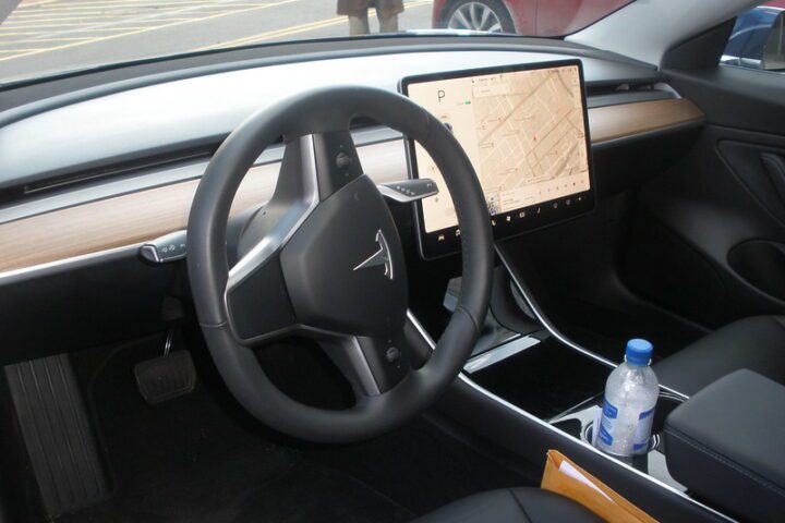 Interior view of a Tesla Model 3 cockpit featuring minimalist dashboard design, touchscreen display, and steering wheel.