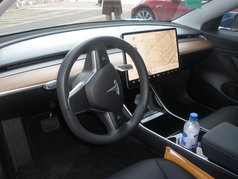 Interior view of a Tesla Model 3 cockpit featuring minimalist dashboard design, touchscreen display, and steering wheel.