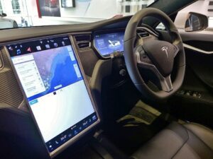 Right‑hand‑drive Tesla Model S interior showing steering wheel, dashboard, and large central touchscreen display turned on with navigation map, photographed in Sydney.