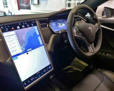 Right‑hand‑drive Tesla Model S interior showing steering wheel, dashboard, and large central touchscreen display turned on with navigation map, photographed in Sydney.