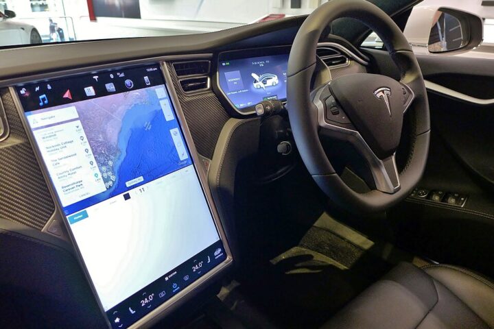 Right‑hand‑drive Tesla Model S interior showing steering wheel, dashboard, and large central touchscreen display turned on with navigation map, photographed in Sydney.