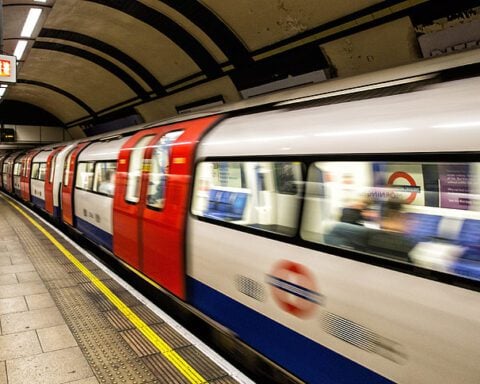 London Underground train arriving at a curved platform with TfL roundel and safety markings visible.