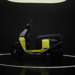 TVS Orbiter electric scooter in matte metallic finish displayed at launch event, positioned in front of large “O” backdrop.