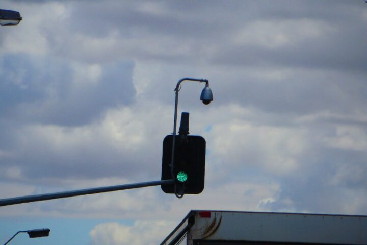 Overhead traffic-signal camera mounted above a green light at an Adelaide intersection, with cloudy sky background.