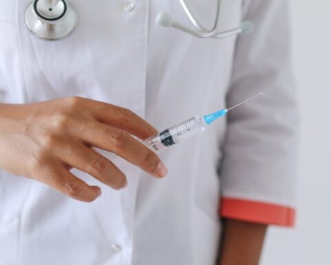 A healthcare professional in a white coat holding a syringe with blue liquid, preparing to administer a vaccination.