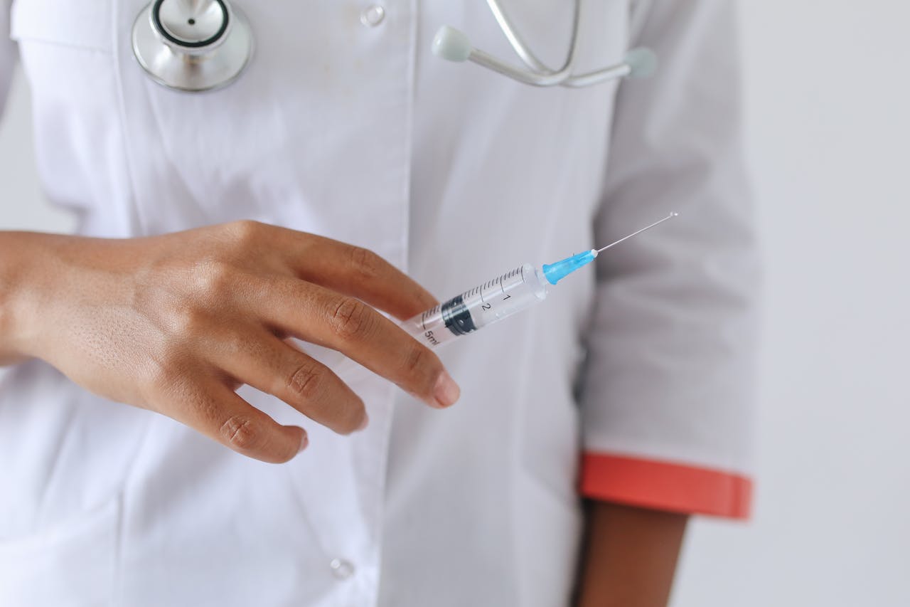 A healthcare professional in a white coat holding a syringe with blue liquid, preparing to administer a vaccination.