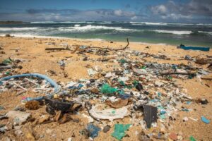 Plastic debris covering a Hawai‘i beach, including bottles, containers, and ropes, with ocean waves visible in the background.