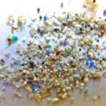 Colorful microplastic particles of various sizes and shapes scattered against a white background, showing the diversity of plastic fragments found in environmental samples.