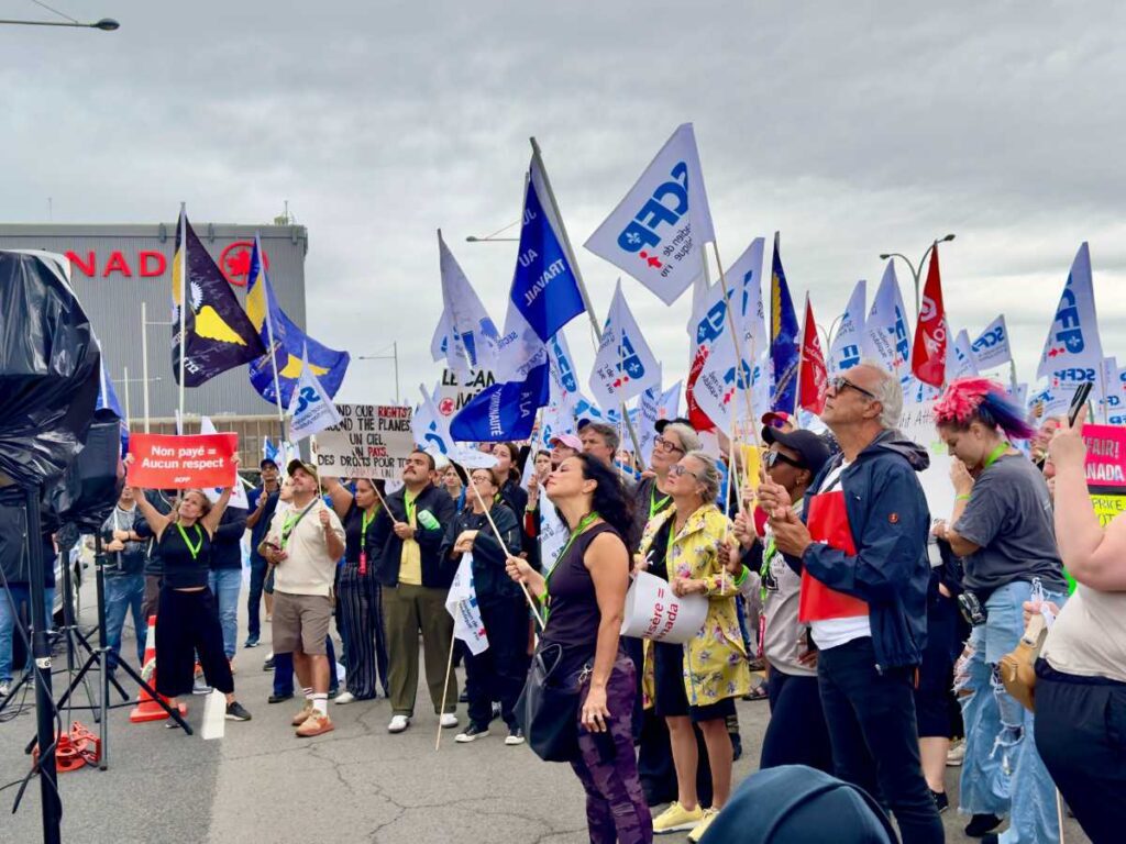 Group of Air Canada flight attendants and union supporters rallying in Montréal with flags and protest signs during the 2025 strike dispute.