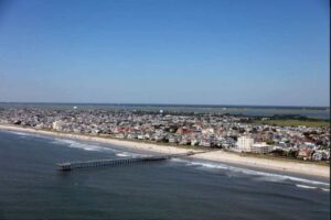 Aerial photograph of Ventnor City, New Jersey shoreline showing beach, ocean waves, residential buildings, and a fishing pier extending into the Atlantic Ocean, taken in 2017.