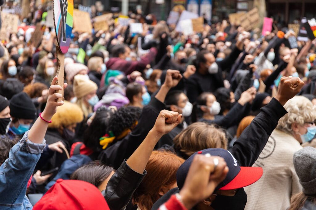 Crowd of protesters with raised fists in solidarity at a demonstration in Melbourne, Australia. Many wear face masks and hold signs, with diverse participants showing unity against discrimination.