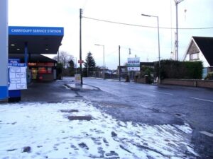 Snow-dusted pavement and a service station on Hillsborough Road, Carryduff, under overcast skies.