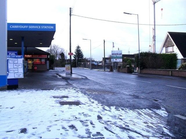 Snow-dusted pavement and a service station on Hillsborough Road, Carryduff, under overcast skies.