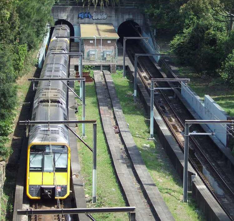 Aerial view of the unfinished Woollahra Station site showing train tracks, platform foundations, and surrounding vegetation between tunnels on Sydney's Eastern Suburbs railway line.