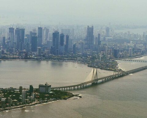 Mumbai skyline featuring high-rise buildings and the Bandra-Worli Sea Link bridge under a hazy sky.