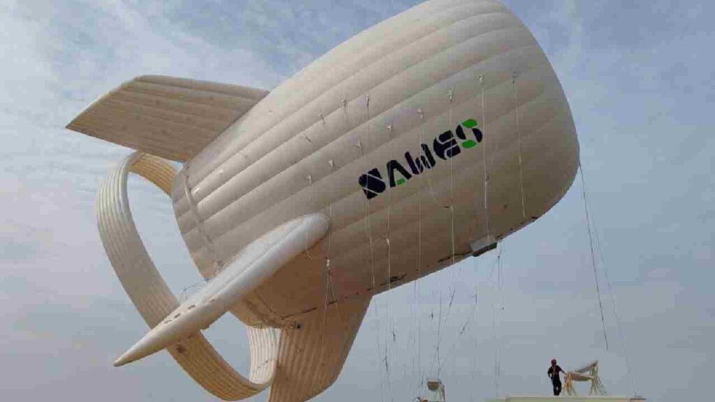White, streamlined XAWind airborne wind turbine tethered to the ground with technicians on a platform, preparing the system for operation.