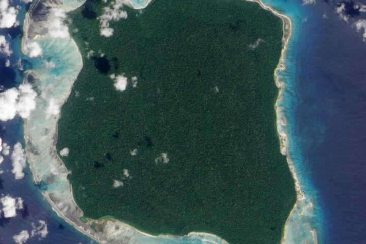 Satellite view of North Sentinel Island in the Andaman Sea, showing forested land surrounded by coral reefs and turquoise waters.