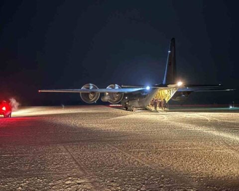 An RNZAF C-130J Hercules sits on a groomed ice runway at McMurdo Station under dark Antarctic skies as crew members stand by the open rear ramp.