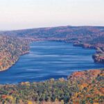 Aerial view of Canadice Lake’s undeveloped, forested shoreline surrounded by autumn foliage in the Finger Lakes region.