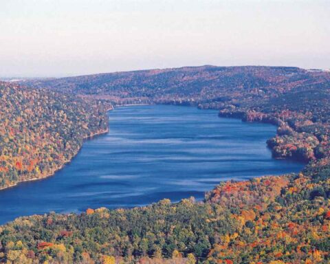 Aerial view of Canadice Lake’s undeveloped, forested shoreline surrounded by autumn foliage in the Finger Lakes region.