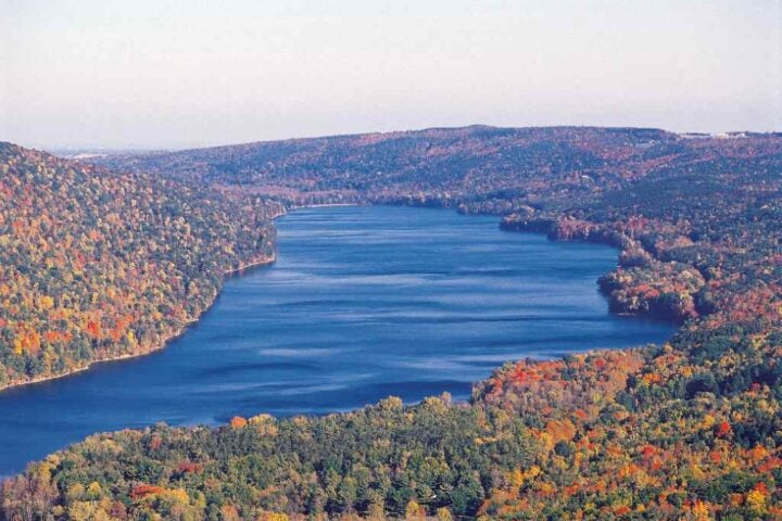 Aerial view of Canadice Lake’s undeveloped, forested shoreline surrounded by autumn foliage in the Finger Lakes region.