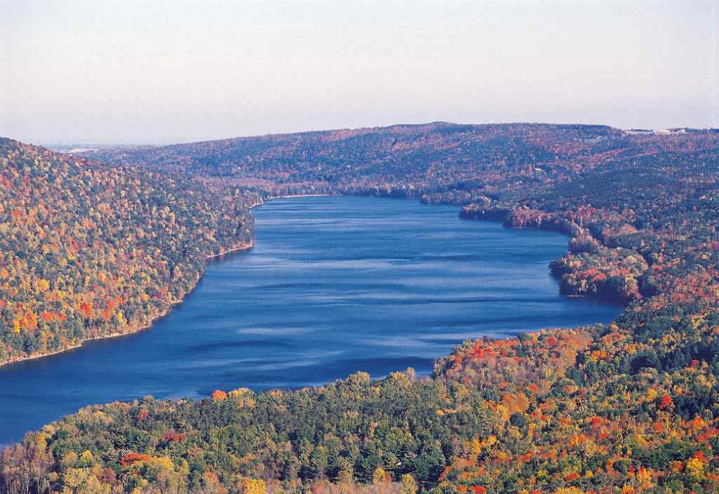 Aerial view of Canadice Lake’s undeveloped, forested shoreline surrounded by autumn foliage in the Finger Lakes region.