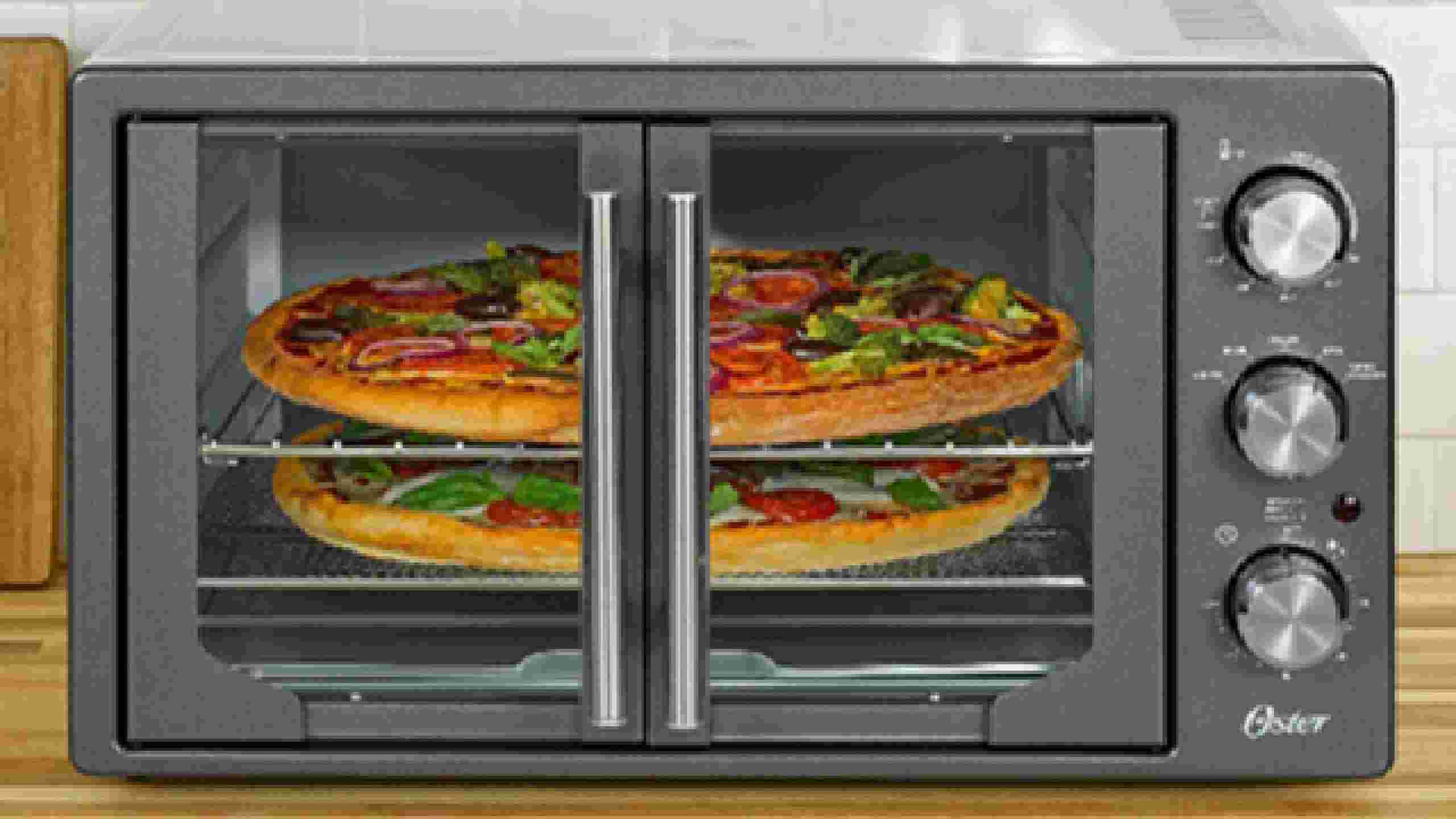 Oster French Door Countertop Oven model TSSTTVFDMAF with stainless steel finish, featuring center-opening glass doors and control knobs on the right side, shown cooking multiple pizzas on two racks.