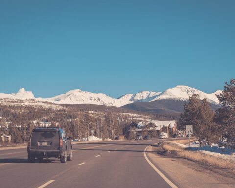A black SUV driving on a mountain highway with snow-capped Rocky Mountains in the background and a speed limit sign of 35 mph visible on the roadside.