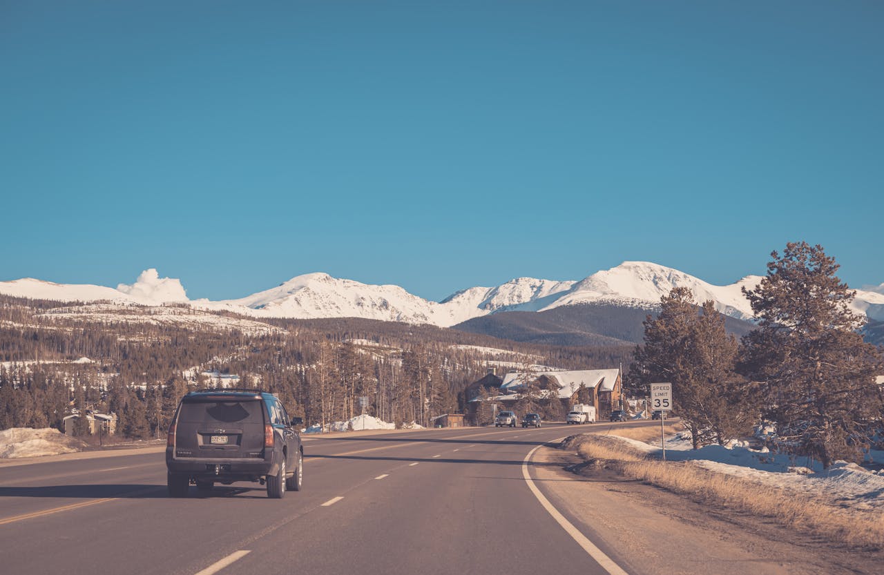 A black SUV driving on a mountain highway with snow-capped Rocky Mountains in the background and a speed limit sign of 35 mph visible on the roadside.