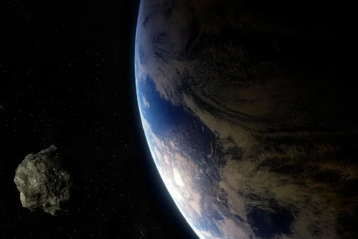 Asteroid approaching Earth against the black background of space, with the blue planet visible in the frame.