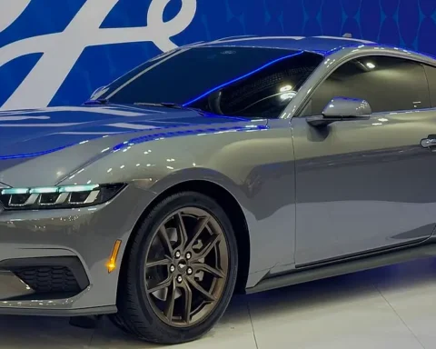 Side-front view of a silver 2024 Ford Mustang coupe with dark wheels displayed at an auto show, featuring the redesigned front end with signature tri-bar LED headlights characteristic of the seventh-generation model.