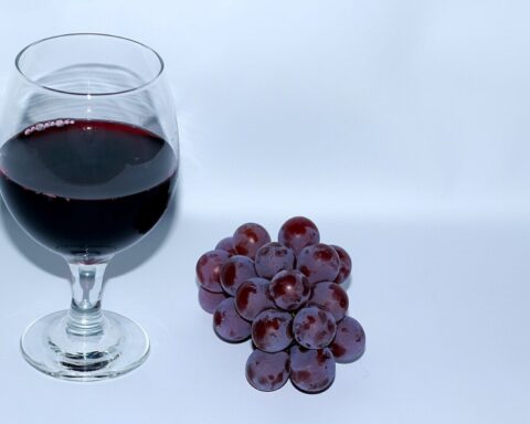 A glass of red wine next to a small bunch of purple grapes (CC BY-SA 3.0)