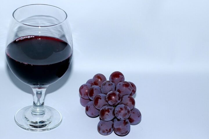 A glass of red wine next to a small bunch of purple grapes (CC BY-SA 3.0)