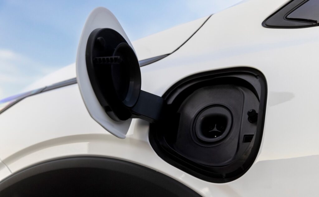 Open electric vehicle charging port with black connector visible on white car exterior