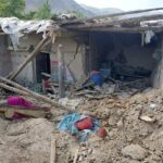 Destroyed house in Afghanistan after an earthquake, showing collapsed walls, exposed wooden beams, and debris scattered on the ground.