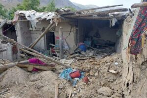 Destroyed house in Afghanistan after an earthquake, showing collapsed walls, exposed wooden beams, and debris scattered on the ground.