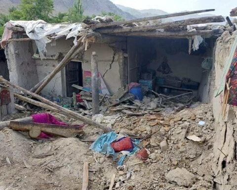 Destroyed house in Afghanistan after an earthquake, showing collapsed walls, exposed wooden beams, and debris scattered on the ground.